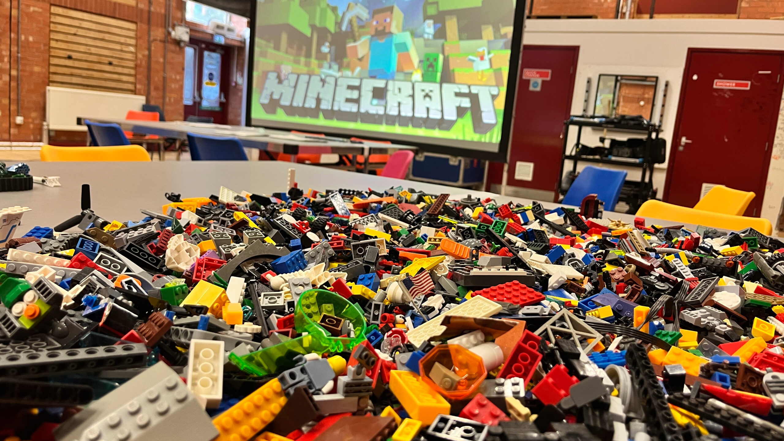 A photo of a table with colourful lego blocks in front of a screen with MINECRAFT written on it.